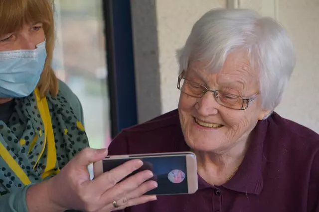 A mid age female caregiver is showing a phone screen to an elderly woman